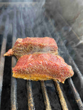 Two seasoned pieces of Bakar Meats Lamb Sirloin on a grill with smoke rising.