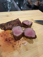 Sliced Bakar Meats lamb tenderloin on a wooden cutting board with a knife