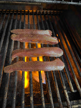 Three pieces of seasoned lamb tenderloin meat on a grill with glowing coals underneath.