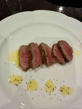 Sliced lamb tenderloin on a white plate with oil and saffron